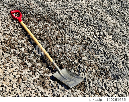 A square shovel stands in front of a pile of crushed stone at an outdoor construction A square shovel stands in front of a pile of crushed stone at an outdoor construction 140261686