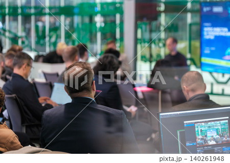 Business professionals attending conference presentation in modern glass meeting room with laptops and screens 140261948