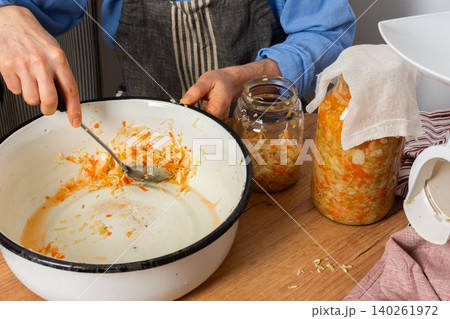 In a kitchen, a 53-year-old man works on fermenting cabbage and carrots. He carefully transfers the mixture into a glass jar for storage and fermentation In a kitchen, a 53-year-old man works on fermenting cabbage and carrots. He carefully transfers the mixture into a glass jar for storage and fermentation 140261972