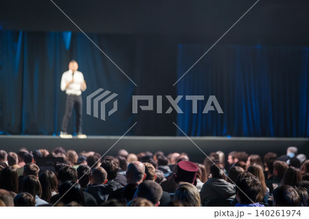 Blurry speaker on stage addressing large audience at conference with dark curtains and spotlight Blurry speaker on stage addressing large audience at conference with dark curtains and spotlight 140261974
