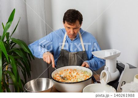 A 53-year-old man mixes cabbage and carrots in a large bowl in his kitchen while preparing for fermentation using simple tools and ingredients 140261988