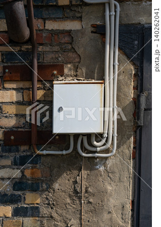 A Weathered Electrical Junction Box Mounted on a Rough Brick Wall Surrounded by Exposed Wires and Industrial Elements in Natural Lighting A Weathered Electrical Junction Box Mounted on a Rough Brick Wall Surrounded by Exposed Wires and Industrial Elements in Natural Lighting 140262041