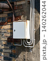 A Detailed Look at an Old Electrical Junction Box Mounted on Weathered Brick Wall with Visible Wiring and Rust Accumulation 140262044