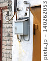 A Rustic Wall-Mounted Mailbox with an Overhead Wire Connection Captured Against a Textured Brick Surface in Natural Light 140262053