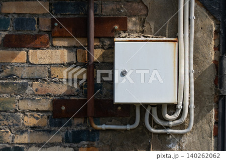 Electrical Junction Box Installed on an Aged Brick Wall Surrounded by Conduits and Metal Fixtures, Showcasing Urban Infrastructure and Maintenance Details 140262062