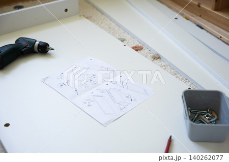 Electric drill and assembly instructions on white surface with screws and tools nearby 140262077