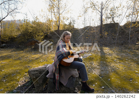 Blonde woman playing string guitar outdoors in autumn forest. Concept of sound therapy, mental health and wellness rituals. Calmness tranquility audio-sensory practices. Aura farming energy Blonde woman playing string guitar outdoors in autumn forest. Concept of sound therapy, mental health and wellness rituals. Calmness tranquility audio-sensory practices. Aura farming energy 140262242