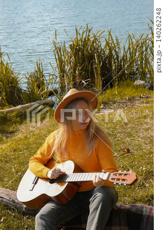 Portrait of smiling caucasian artist plays wooden acoustic guitar in autumnal park. Young songwriter plays string musical instrument hobby outside in nature fall time. Audio music healing 140262248