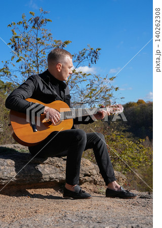 Blonde man playing string guitar outdoors in autumn forest. Concept of sound therapy, mental health and wellness rituals. Calmness tranquility audio-sensory practices. Aura farming energy Blonde man playing string guitar outdoors in autumn forest. Concept of sound therapy, mental health and wellness rituals. Calmness tranquility audio-sensory practices. Aura farming energy 140262308