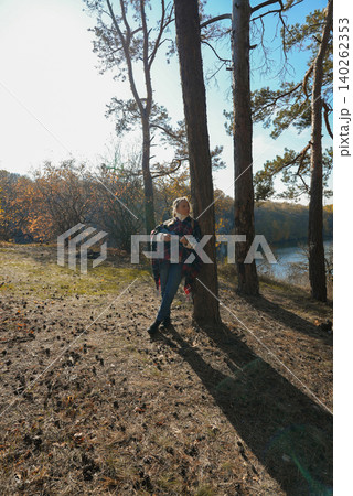 Beautiful blonde girl playing guitar ukulele and singing relaxing enjoying outdoors on sunny autumn day. Hippie woman in boho style training playing musical instrument. Fall leaves Beautiful blonde girl playing guitar ukulele and singing relaxing enjoying outdoors on sunny autumn day. Hippie woman in boho style training playing musical instrument. Fall leaves 140262353