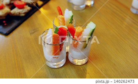 Shot glasses containing creamy dip garnished with colorful vegetable sticks carrot, cucumber, bell pepper, daikon radish presenting appetizing healthy snack on rustic wooden surface Shot glasses containing creamy dip garnished with colorful vegetable sticks carrot, cucumber, bell pepper, daikon radish presenting appetizing healthy snack on rustic wooden surface 140262473