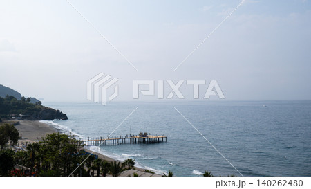 Waves crashing on wooden pier in Antalya Turkey. Palms and sea vacation travel tourism scene concept. Sandy beach and mountains Waves crashing on wooden pier in Antalya Turkey. Palms and sea vacation travel tourism scene concept. Sandy beach and mountains 140262480