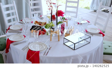 Elegant round dining setup with crisp white tablecloth, pristine dinnerware, sparkling glassware, and vibrant red rose centerpiece enhancing celebratory table design Elegant round dining setup with crisp white tablecloth, pristine dinnerware, sparkling glassware, and vibrant red rose centerpiece enhancing celebratory table design 140262525