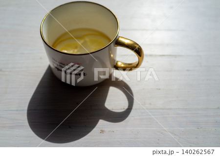 White mug with lemon tea and shadow on wooden table White mug with lemon tea and shadow on wooden table 140262567