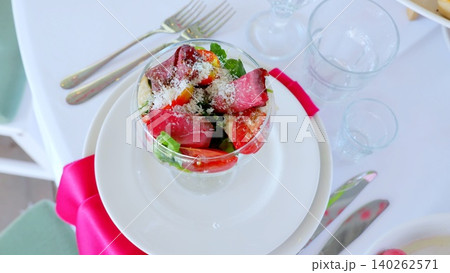 Refined dining setup displaying savory beef salad with tomatoes, arugula, parmesan nestled in white ceramic plate alongside polished silverware, soft pink linen napkin Refined dining setup displaying savory beef salad with tomatoes, arugula, parmesan nestled in white ceramic plate alongside polished silverware, soft pink linen napkin 140262571