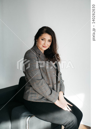 Beautiful brunette woman sitting on chair and smiling. Portrait of a woman with dark hair. Business woman. Plus size model. Beautiful brunette woman sitting on chair and smiling. Portrait of a woman with dark hair. Business woman. Plus size model. 140262630