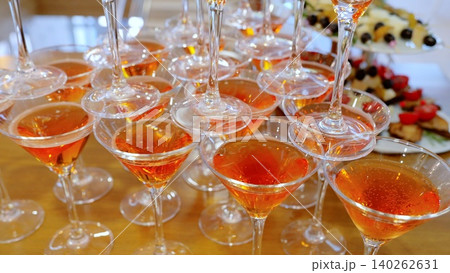 Martini glasses pyramided with orange aperol spritz, spilling over celebratory appetizers during festive party gathering Martini glasses pyramided with orange aperol spritz, spilling over celebratory appetizers during festive party gathering 140262631