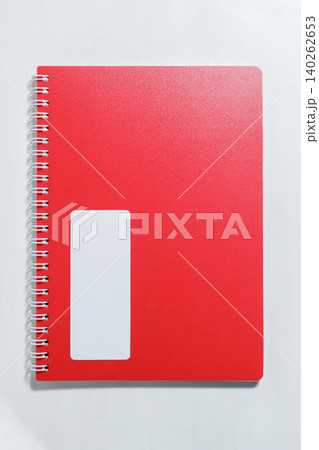 Bright red notebook cover features smooth texture. White rectangular label appears on the front. Silver spiral binding holds the notebook securely. High quality photo 140262653