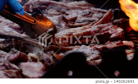 Grilling professional wearing protective gloves flipping juicy barbecue ribs over sizzling flames, producing mouthwatering outdoor cooking display Grilling professional wearing protective gloves flipping juicy barbecue ribs over sizzling flames, producing mouthwatering outdoor cooking display 140262691