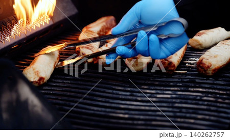 Grilling sausages with metal tongs, professional chef managing flame kissed meat during outdoor summer barbecue celebration, smoke rising intensely Grilling sausages with metal tongs, professional chef managing flame kissed meat during outdoor summer barbecue celebration, smoke rising intensely 140262757