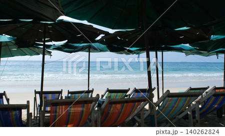 Rows of empty colorful beach umbrellas and lounge chairs set up on sandy beach facing calm sea. Beach resort concept 140262824