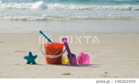 Colorful children's sand play set with molds, shovel, bucket and rake on sandy beach with gentle sea waves in background. Childhood play concept 140262830
