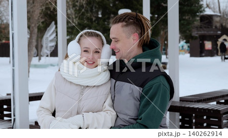 Winter park gazebo framing smiling young couple, wearing warm clothing, embracing snowy landscape with bare trees and soft white scenery surrounding happy partners Winter park gazebo framing smiling young couple, wearing warm clothing, embracing snowy landscape with bare trees and soft white scenery surrounding happy partners 140262914