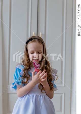 Close-up of a blonde woman holding a pink macaron and enjoying it; braided hair, headband, blue frilly dress, and white apron; soft skin tones; shallow depth of field; bright neutral colors Close-up of a blonde woman holding a pink macaron and enjoying it; braided hair, headband, blue frilly dress, and white apron; soft skin tones; shallow depth of field; bright neutral colors 140263260