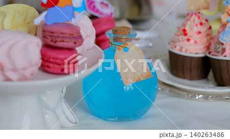 Pastel Dessert Display With Macarons, Bottle Softfocus Tabletop Scene With Macarons On White Cake Stand, Blue Corked Bottle With Blank Tag, Cupcakes With Pink Frosting, Airy Bokeh Background, Styled Pastel Dessert Display With Macarons, Bottle Softfocus Tabletop Scene With Macarons On White Cake Stand, Blue Corked Bottle With Blank Tag, Cupcakes With Pink Frosting, Airy Bokeh Background, Styled 140263486