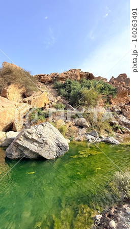 Sunny Stream With Rocky Terrain. Bright Flowing Water Beside Rugged Stone Formations. Vibrant Stream Cascading Past Sundappled Rocks And Hardy Plants Along Rugged Landscape Sunny Stream With Rocky Terrain. Bright Flowing Water Beside Rugged Stone Formations. Vibrant Stream Cascading Past Sundappled Rocks And Hardy Plants Along Rugged Landscape 140263491