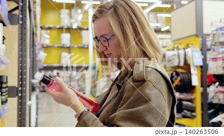 Customer making a decision on purchasing red shampoo bottle while browsing beauty and hygiene products in supermarket aisle Customer making a decision on purchasing red shampoo bottle while browsing beauty and hygiene products in supermarket aisle 140263506