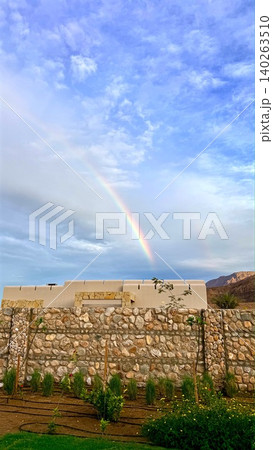 Vivid Sky Scene. Colorful Arch Above Rustic Landscape. Bright Rainbow Arches Over Tranquil Countryside. Spectrum Of Colors Spans Sky Above Peaceful Vineyard And Hills 140263510