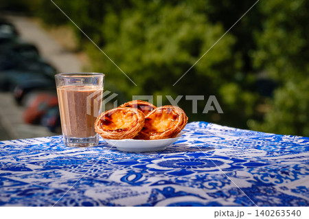 Portuguese custard tarts and coffee with pastel de nata on a blue table in warm outdoor light and blurred background. Famous regional delicacy, cultural food, travel cuisine Portuguese custard tarts and coffee with pastel de nata on a blue table in warm outdoor light and blurred background. Famous regional delicacy, cultural food, travel cuisine 140263540