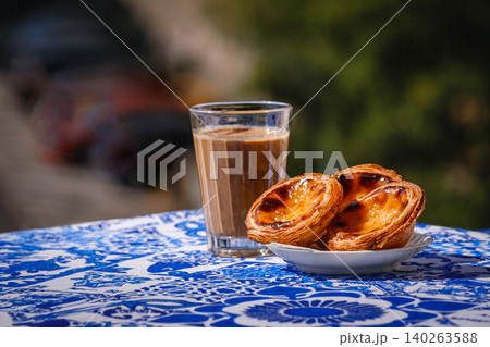Portuguese custard tarts and coffee with pastel de nata on a blue table in a sunny outdoor food setting. Famous pastry, regional delicacy, cultural food, travel cuisine Portuguese custard tarts and coffee with pastel de nata on a blue table in a sunny outdoor food setting. Famous pastry, regional delicacy, cultural food, travel cuisine 140263588