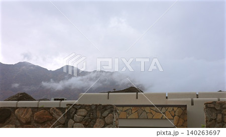 Cloudy Mountain View. Foggy Peaks Behind Quiet Roof. Silent Skyline With Distant Mountain Silhouettes. Serene Horizon Framed By Modern Building And Misty Clouds Cloudy Mountain View. Foggy Peaks Behind Quiet Roof. Silent Skyline With Distant Mountain Silhouettes. Serene Horizon Framed By Modern Building And Misty Clouds 140263697