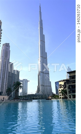 Luxury Skyscraper With Reflective Pools. Tall Building With Shimmering Water Surroundings. Majestic Structure Overlooking Serene Water Areas Under Vibrant Clear Blue Sky Luxury Skyscraper With Reflective Pools. Tall Building With Shimmering Water Surroundings. Majestic Structure Overlooking Serene Water Areas Under Vibrant Clear Blue Sky 140263710