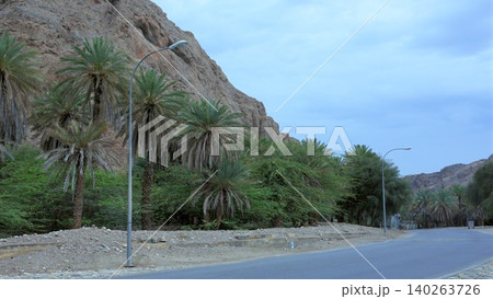 Mountain Road Adventure. Travelers Explore Peaceful Mountain Pathways During Sunset Hours. Traveler Searches For Tranquil Roads Among Towering Rocks And Lush Palm Trees Mountain Road Adventure. Travelers Explore Peaceful Mountain Pathways During Sunset Hours. Traveler Searches For Tranquil Roads Among Towering Rocks And Lush Palm Trees 140263726