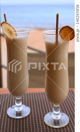 Refreshing Tropical Banana Beverage In Sunlight. Enjoy Cool Banana Smoothie With Ocean View Backdrop. Tropical Banana Smoothies In Tall Glasses With Ocean And Sunlight Ambiance Refreshing Tropical Banana Beverage In Sunlight. Enjoy Cool Banana Smoothie With Ocean View Backdrop. Tropical Banana Smoothies In Tall Glasses With Ocean And Sunlight Ambiance 140263856