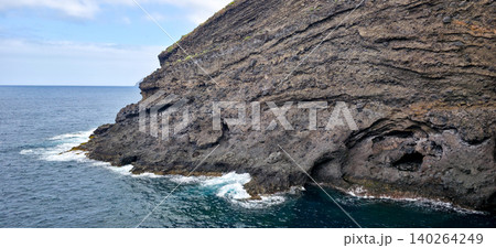 Rocky coastline with dark volcanic rocks and clear blue ocean waves lapping against the shore in a coastal landscape. High quality photo 140264249
