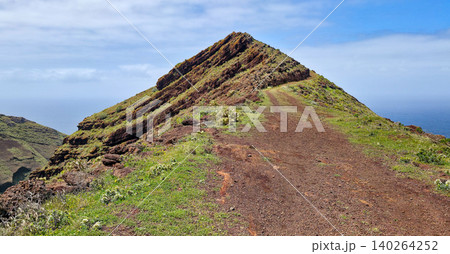 Scenic view of a winding dirt path leading up a green hillside overlooking the ocean in a coastal landscape. Northern viewpoint of La Palma Island Cruz de La Centinela. High quality photo 140264252