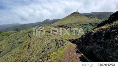 Scenic view of green hills with winding dirt path leading to wind turbines atop a mountain in a rural landscape. High quality photo Scenic view of green hills with winding dirt path leading to wind turbines atop a mountain in a rural landscape. High quality photo 140264258