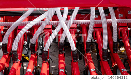 Detailed view of a red farm machine with white corrugated hoses, metal tubes, bolts, and numbered parts arranged in a dense mechanical assembly under bright daylight Detailed view of a red farm machine with white corrugated hoses, metal tubes, bolts, and numbered parts arranged in a dense mechanical assembly under bright daylight 140264311