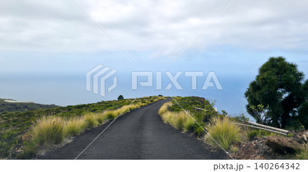 Scenic winding road through lush green landscape with volcanic rock formations under cloudy sky in mountainous region. High quality photo 140264342