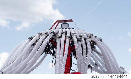 Red industrial equipment fitted with numerous flexible white hoses and cables is shown from a low angle against a bright blue sky with clouds, creating a technical outdoor Red industrial equipment fitted with numerous flexible white hoses and cables is shown from a low angle against a bright blue sky with clouds, creating a technical outdoor 140264401