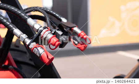 Closeup of black hydraulic hoses with metal fittings and red protective caps attached to industrial equipment, with a blurred yellow background and soft indoor lighting Closeup of black hydraulic hoses with metal fittings and red protective caps attached to industrial equipment, with a blurred yellow background and soft indoor lighting 140264421