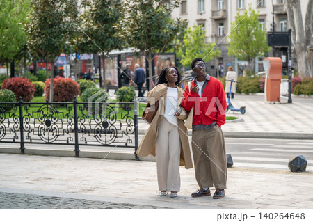Smiling positive african american man and woman friends enjoying modern city area on daily walk Smiling positive african american man and woman friends enjoying modern city area on daily walk 140264648