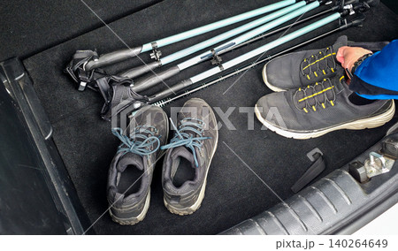 Hiking gear including trekking poles and two pairs of shoes arranged in the trunk of a vehicle, ready for outdoor adventure and exploration. High quality photo Hiking gear including trekking poles and two pairs of shoes arranged in the trunk of a vehicle, ready for outdoor adventure and exploration. High quality photo 140264649