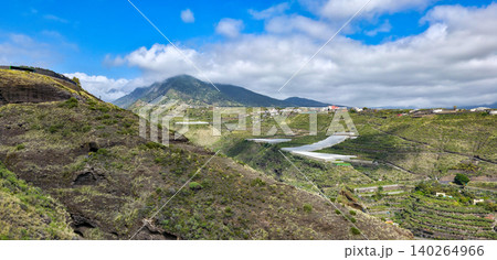 Scenic view of terraced green hillsides leading down to the ocean, with a winding road visible along the landscape under a partly cloudy sky. High quality photo Scenic view of terraced green hillsides leading down to the ocean, with a winding road visible along the landscape under a partly cloudy sky. High quality photo 140264966
