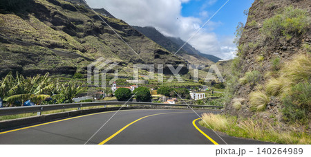 Scenic road winding through lush banana plantations with steep mountainous terrain under a partly cloudy sky in a tropical landscape. High quality photo Scenic road winding through lush banana plantations with steep mountainous terrain under a partly cloudy sky in a tropical landscape. High quality photo 140264989
