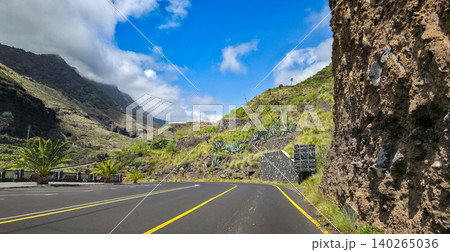 Scenic road winding through lush banana plantations with steep mountainous terrain under a partly cloudy sky in a tropical landscape. High quality photo Scenic road winding through lush banana plantations with steep mountainous terrain under a partly cloudy sky in a tropical landscape. High quality photo 140265036